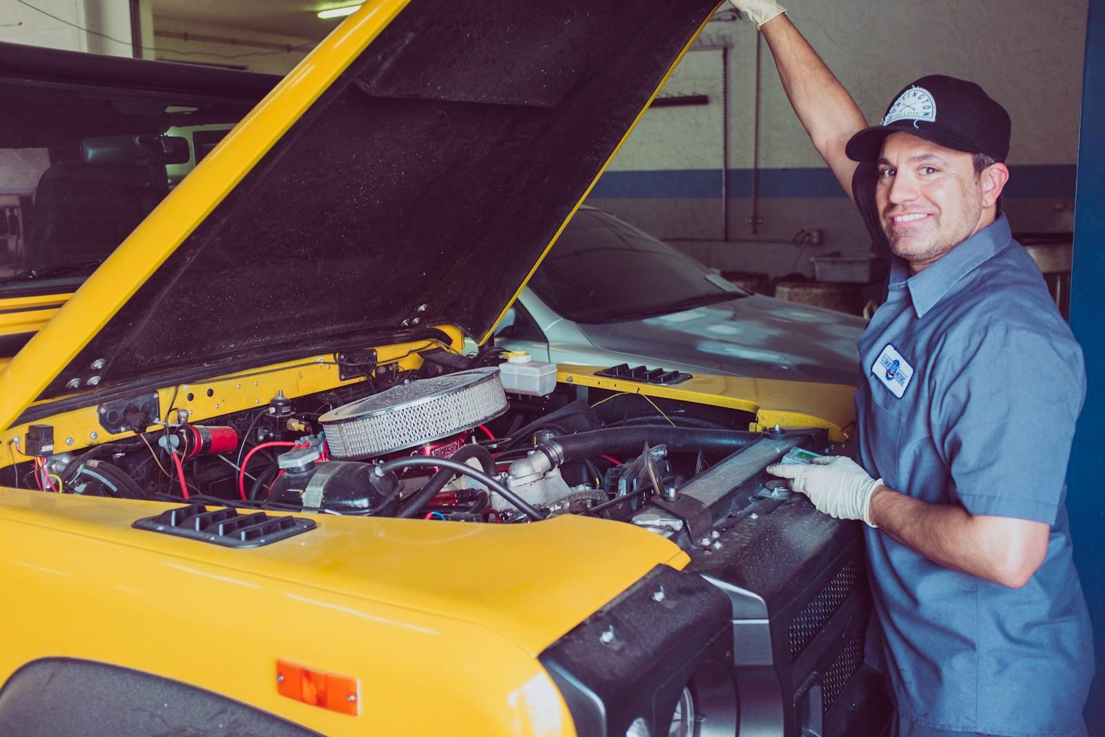 A smiling mechanic with the hood up on a bright yellow car